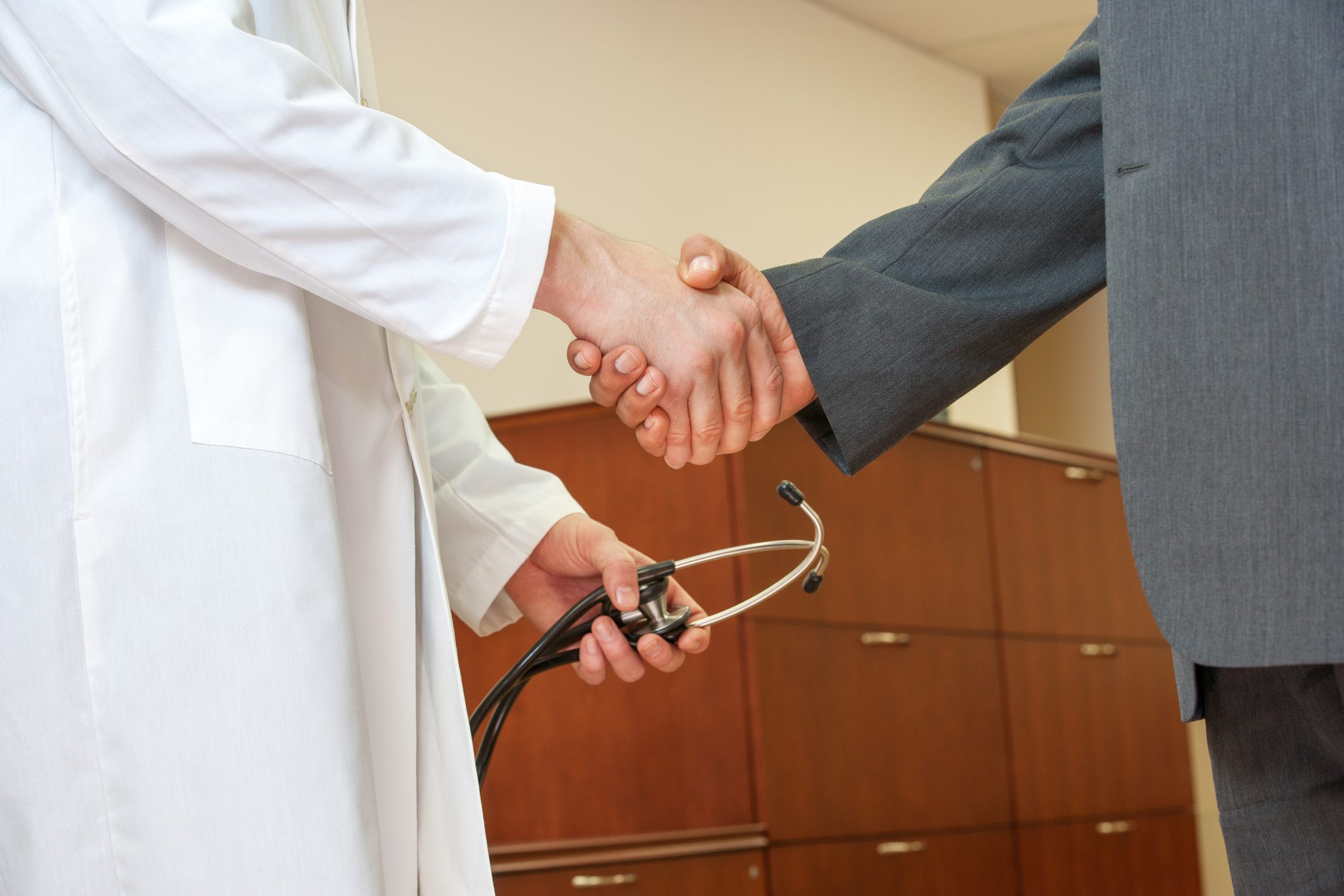 Doctor and businessman shaking hands, holding stethoscope.
