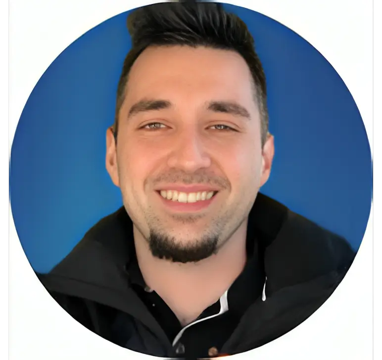 Smiling man in black jacket, blue background.